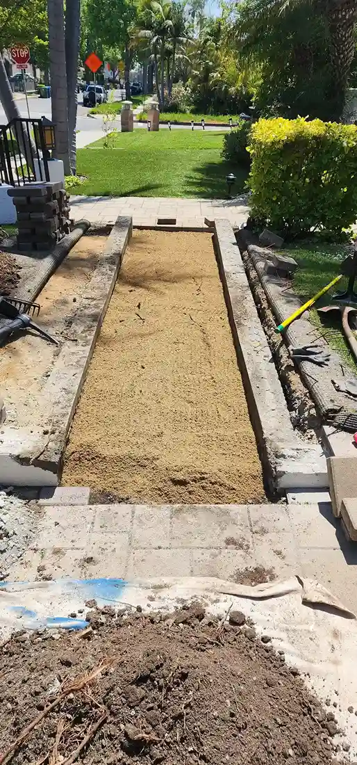 Backyard paver patio installation in progress with sand base and concrete edging by DJ Luxury Renovations