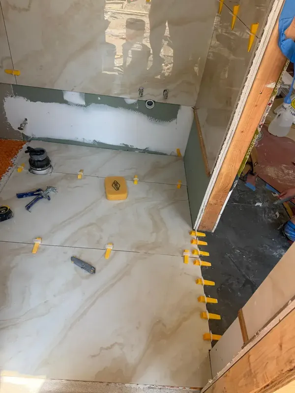Bathroom shower tile installation in progress with leveling clips and tools