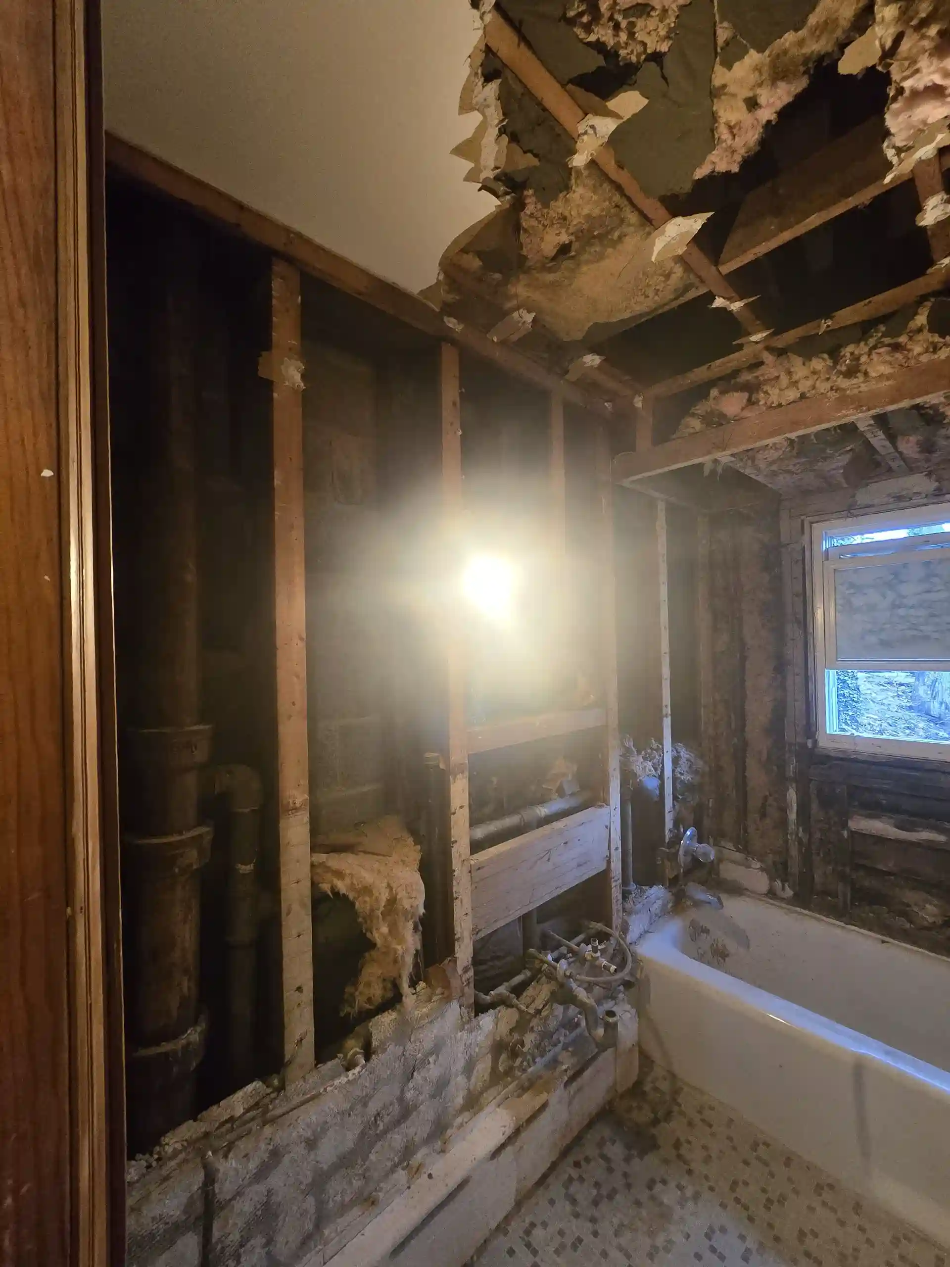 Gutted bathroom during renovation with exposed framing, plumbing and damaged ceiling