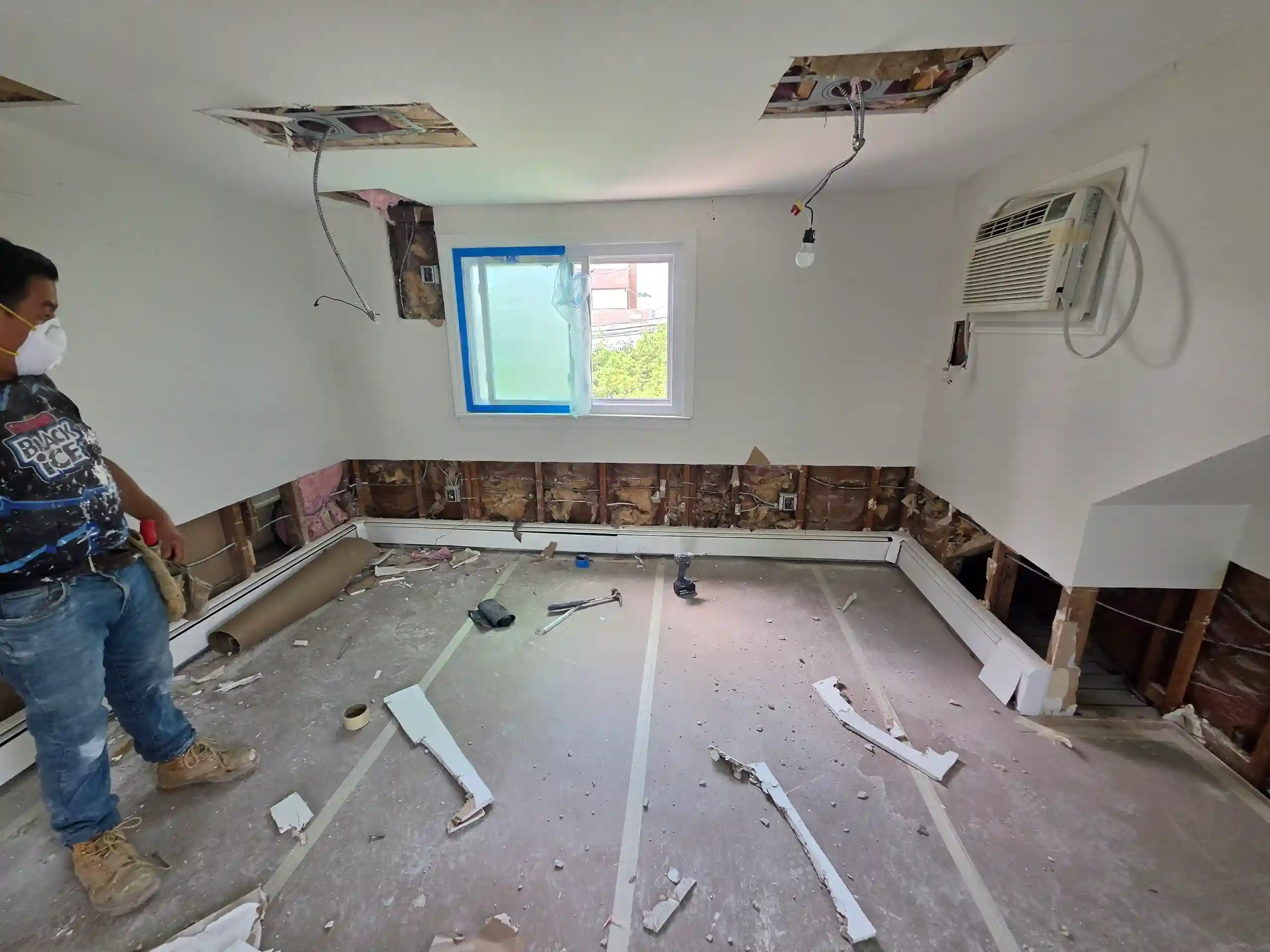 Interior home renovation in progress, worker gutting room with exposed walls and ceiling for remodel