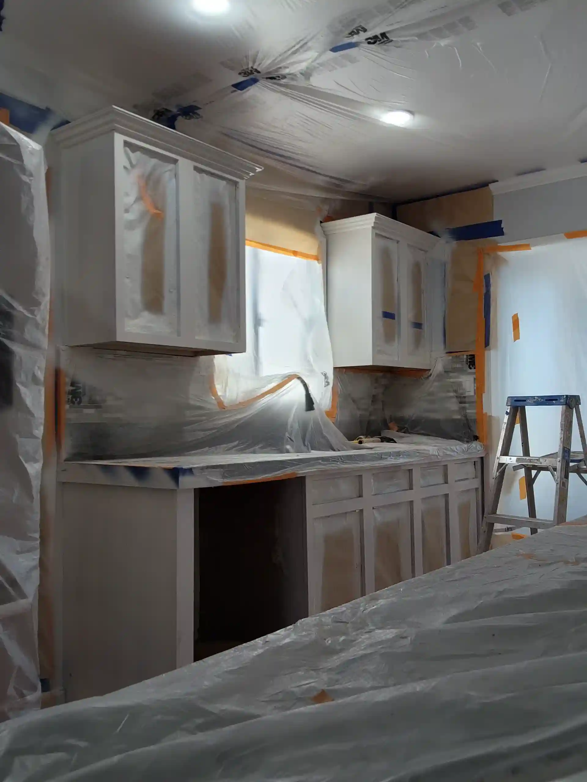 Kitchen renovation before painting with cabinets and counters covered in protective plastic sheeting