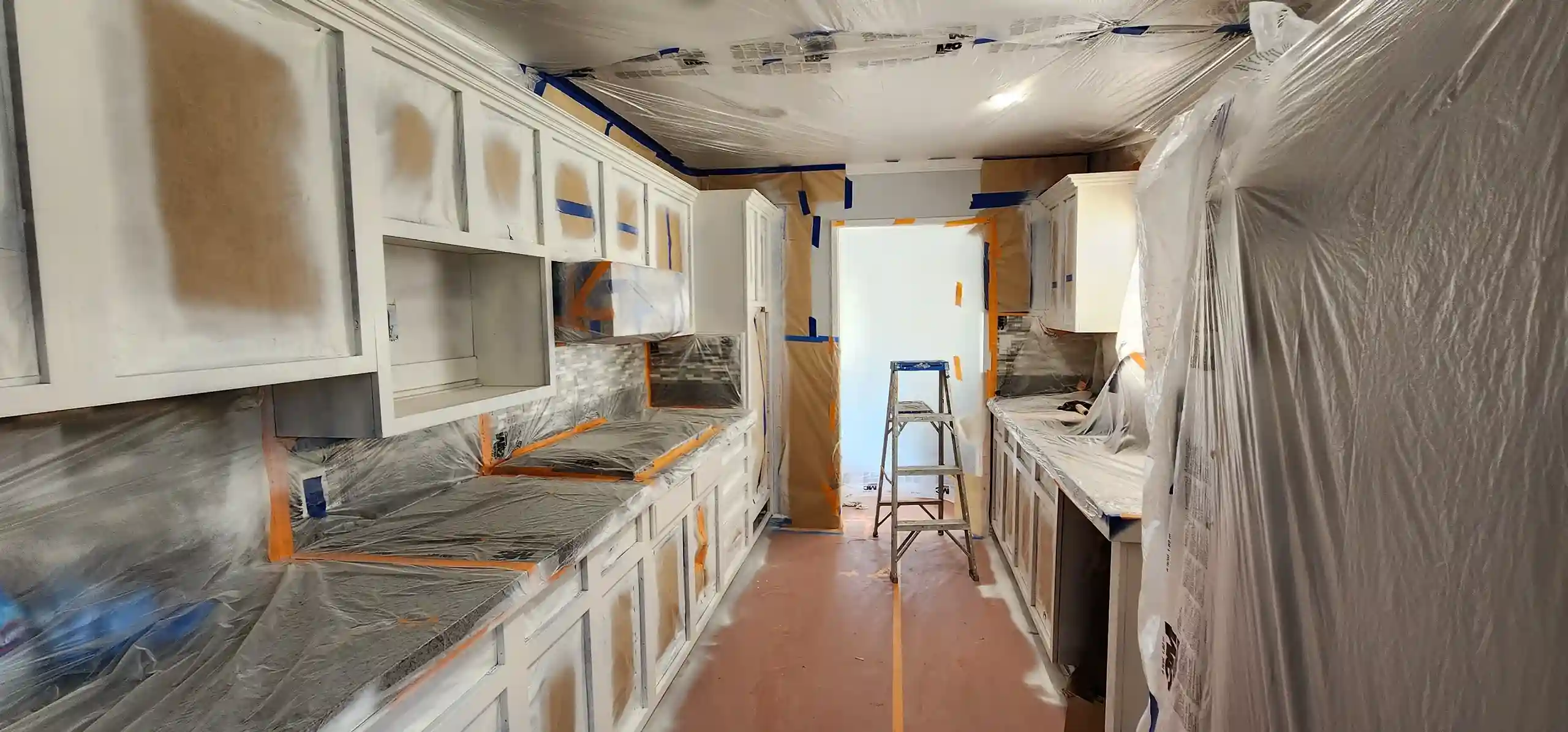 Kitchen under renovation with cabinets, plastic sheeting and ladder in Brooklyn NY home
