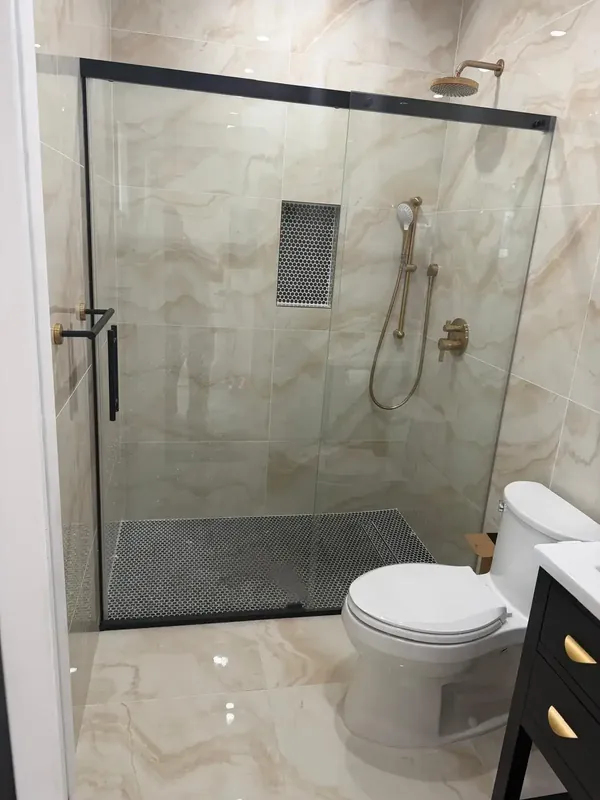 Modern bathroom with glass walk-in shower, marble tile and gold fixtures