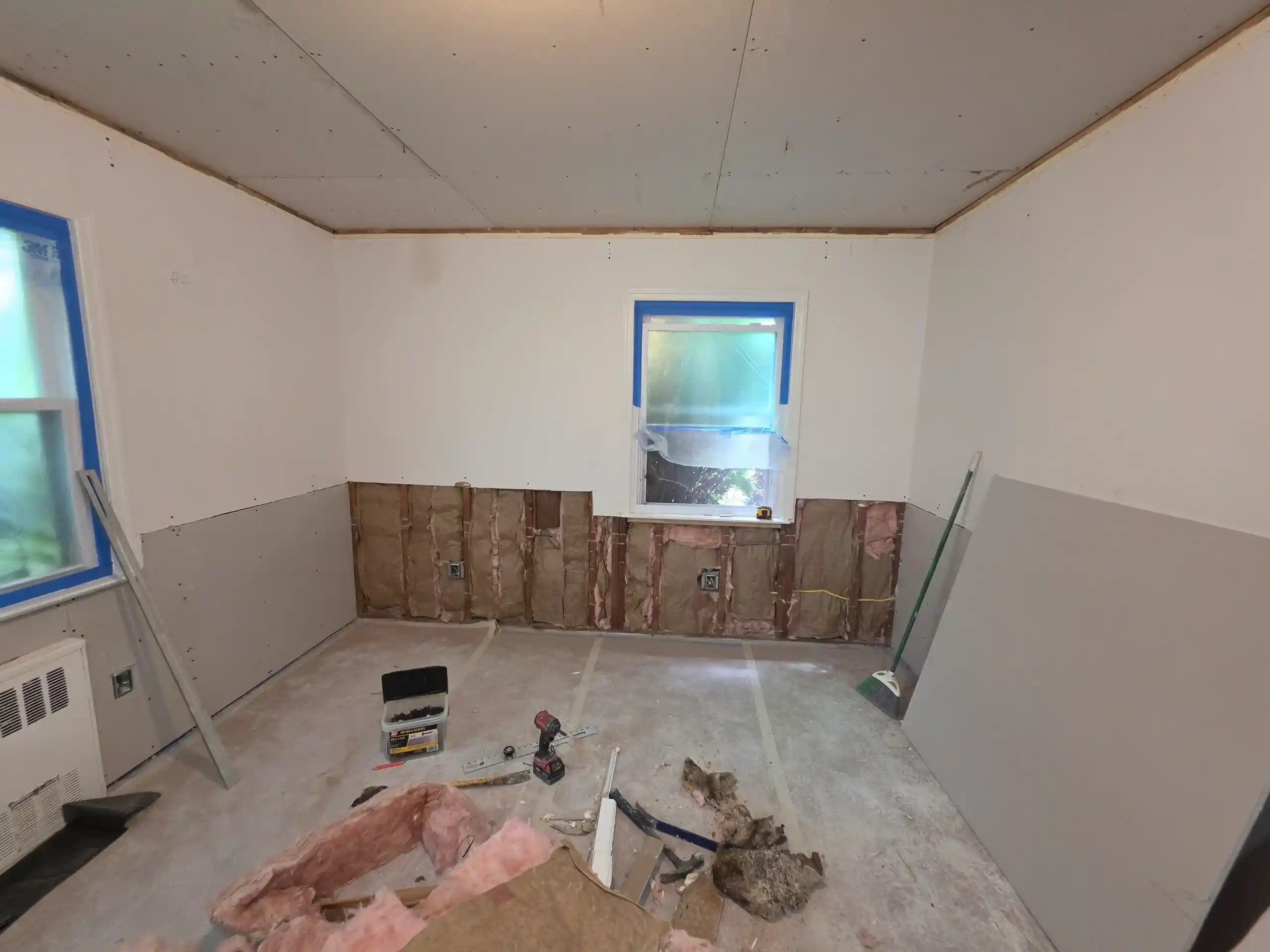 Room renovation in progress with new drywall, exposed insulation and tools on the floor