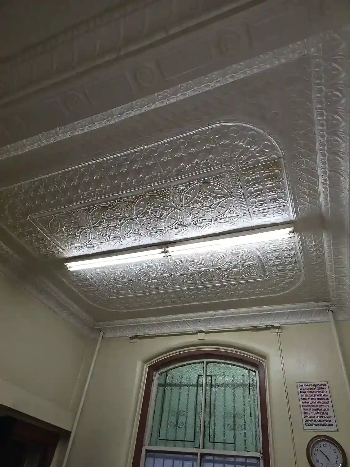 Ornate vintage pressed tin ceiling with fluorescent light before renovation in Brooklyn