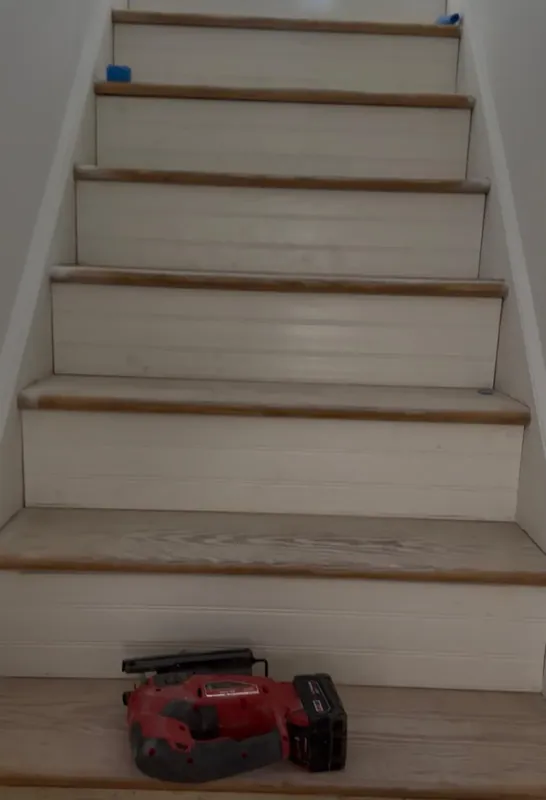 Wooden staircase with white risers under construction with caulking gun